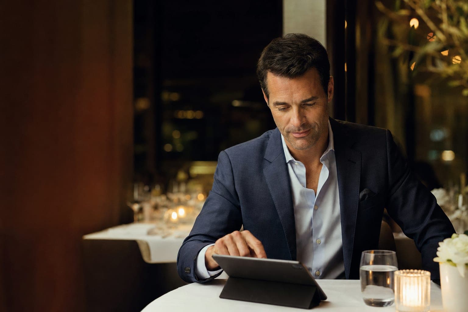 A Clinical Informatician reading on a tablet at a corner table in a fine dining restaurant
