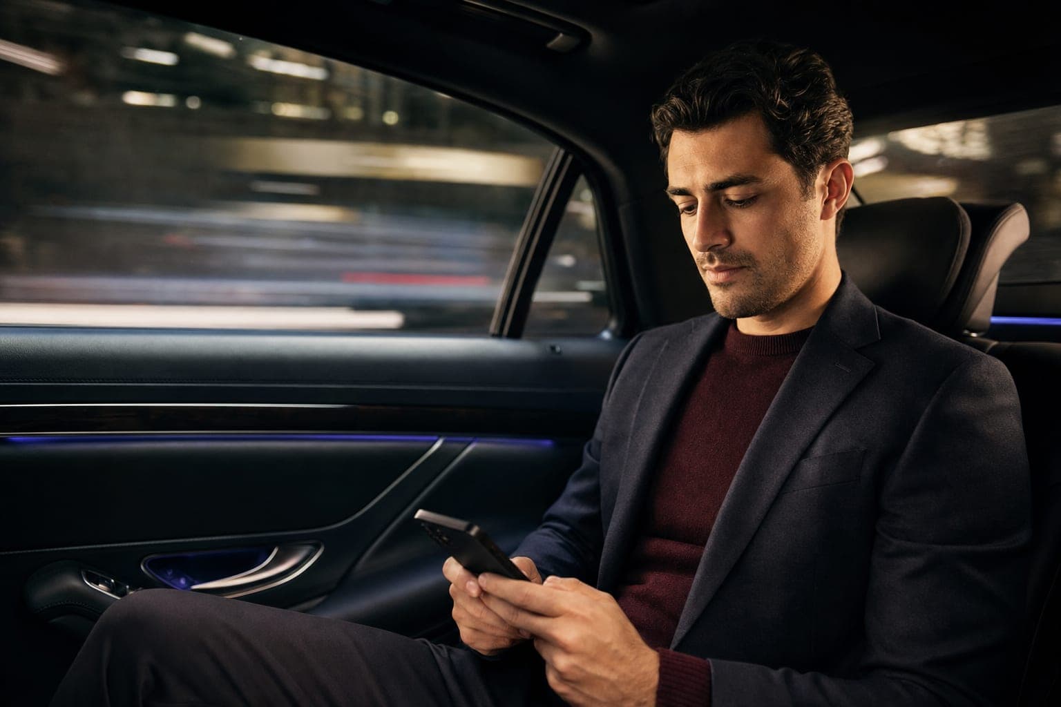 An Internist looking down at a phone in the back seat of a chauffeured car