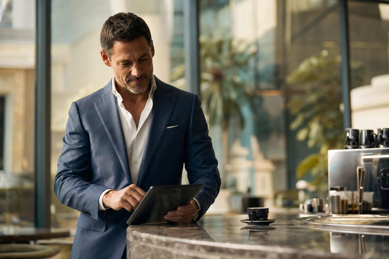 A Nephrologist reading on a tablet at a marble espresso bar in a glass atrium